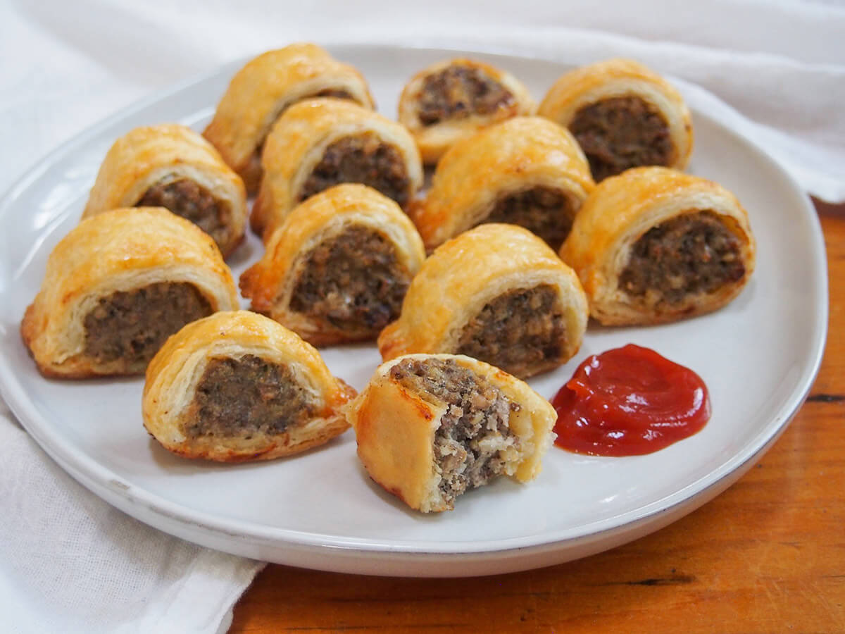 These haggis sausage rolls are a great way to use leftover haggis, introduce people to the flavors of haggis in a milder form, or just as an excuse to have a tasty savory snack! plate with haggis sausage rolls with one bitten one at front and ketchup to side
