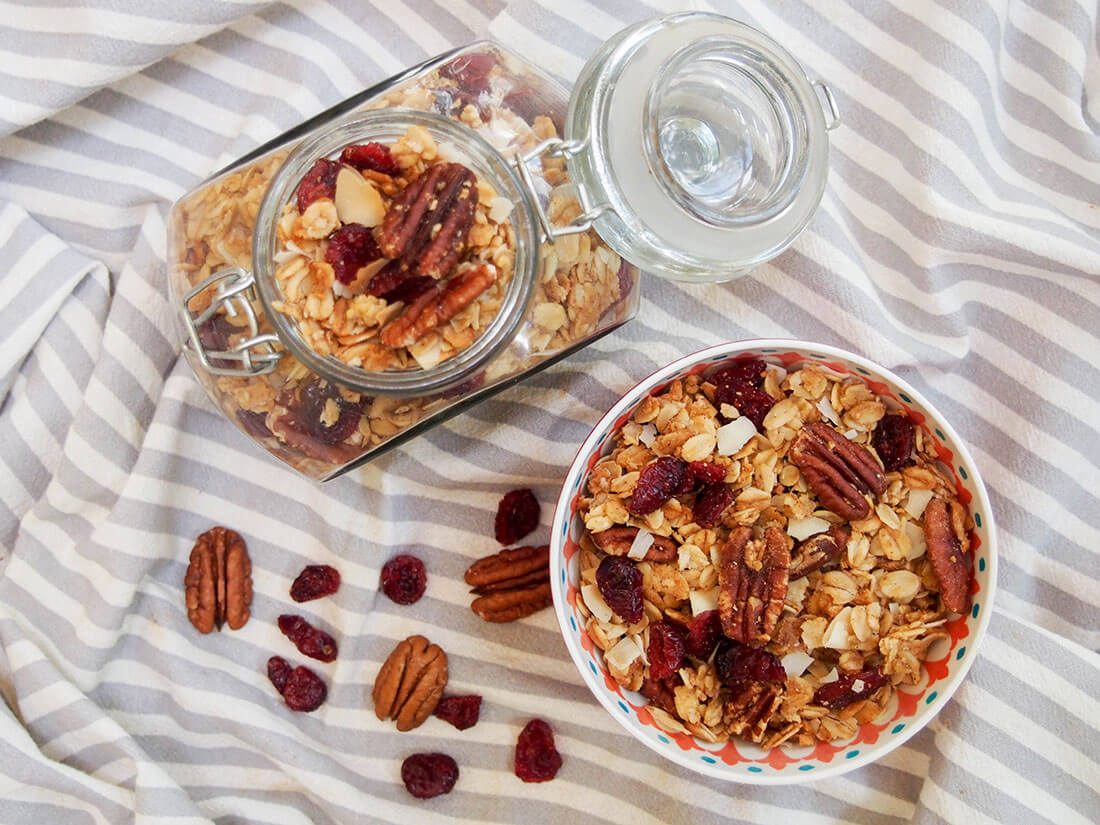 It's easier than you might think to make granola (and healthier). This easy homemade granola recipe is naturally sweetened and loaded up with cranberries, pecans and coconut. Homemade granola recipe - some in bowl, rest in jar from overhead