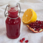 bottle of homemade grenadine with lemon and pomegranate to side