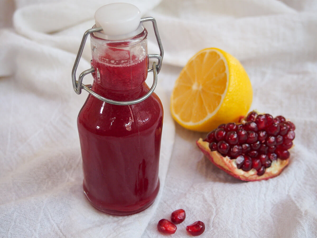 Homemade grenadine is easy to make and so much better than the bought versions. It's packed with bright color and flavor, and perfect to use in a range of cocktails and more. small bottle of homemade grenadine with half lemon and piece of pomegranate to side