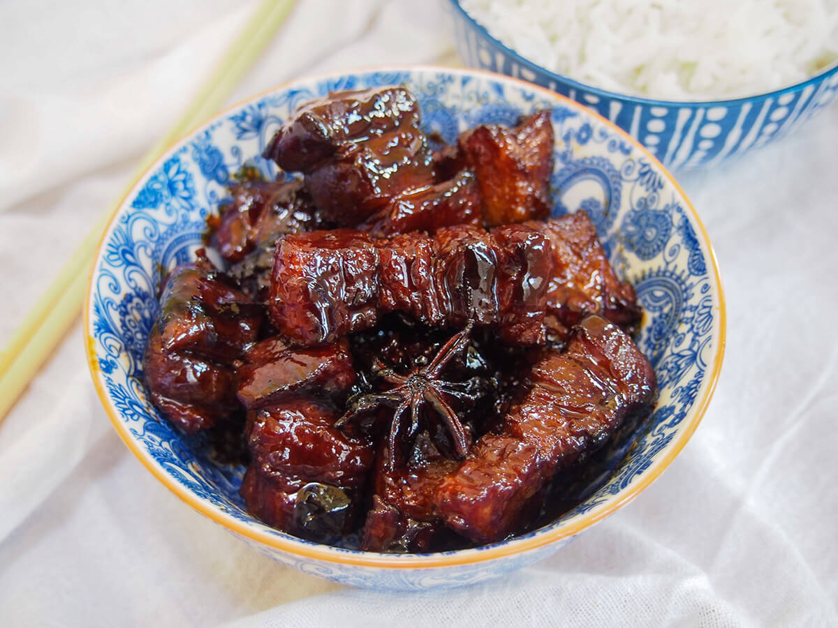 Hong shao rou is a classic Chinese way to prepare pork belly. It's slow braised in a gently sweet and aromatic mixture to make a sticky, tender and wonderfully flavorful dish. side view of bowl of Hong shao rou red braised pork belly