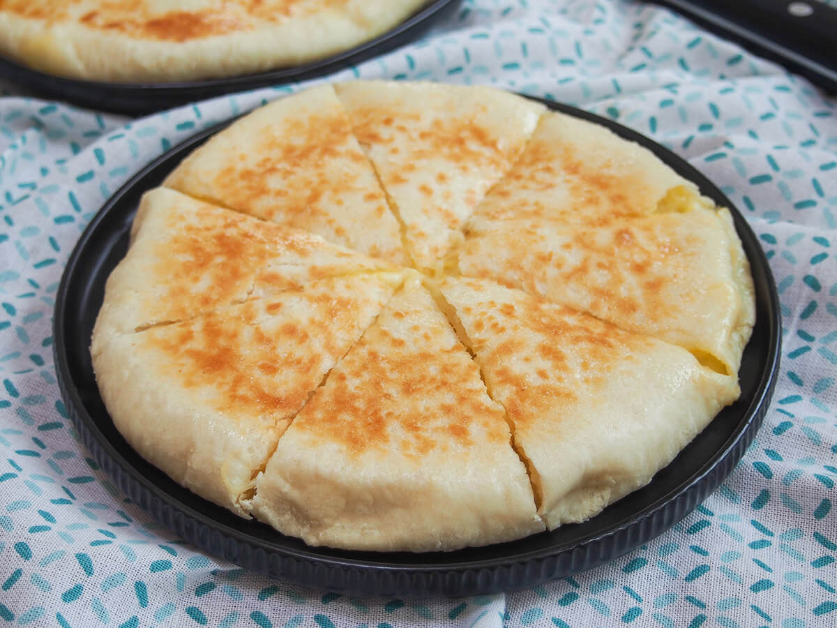 Imeruli khachapuri is a delicious cheese filled bread that's easy to make. It's a simple bread base with oozing cheese inside after a quick cook. Great for sharing, as a snack or part of lunch. imeruli khachapuri on black plate