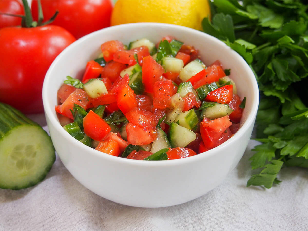 Israeli salad is an easy, crunchy and delicious tomato cucumber salad bowl of Israeli salad with cucumber and tomato one side and parsley bunch to right