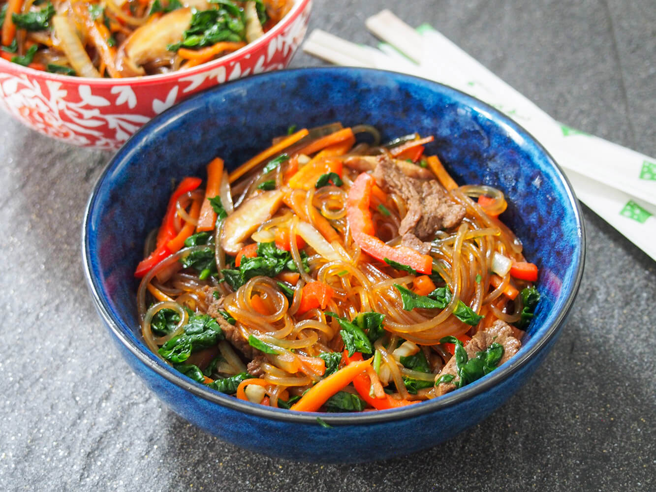 Japchae is an easy and delicious stir fry with a simple seasoning, plenty of vegetables and slightly chewy sweet potato starch noodles. It's both comforting and relatively light, making it the perfect quick meal. blue bowl filled with japchae (Korean glass noodle stir fry)
