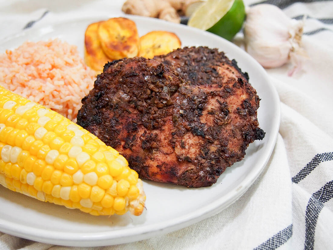 Jerk chicken is a delicious Jamaican dish, perfect for cooking on the grill. With an aromatic marinade, and a little or a lot of spice, it's full of flavor and this recipe makes it easy too! Jamaican jerk chicken with sides of corn, rice and plantain