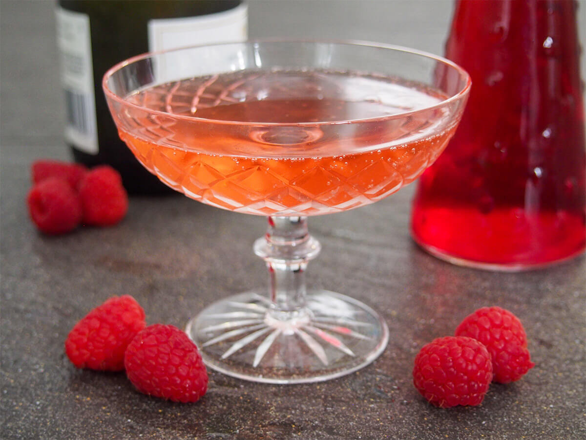 Kir Imperial is a super-simple raspberry champagne cocktail. A variation on the Kir Royale, but with raspberry liqueur, it's bright, bubbly and perfect for a special occasion. glass of kir imperial raspberry champagne cocktail with bottles behind