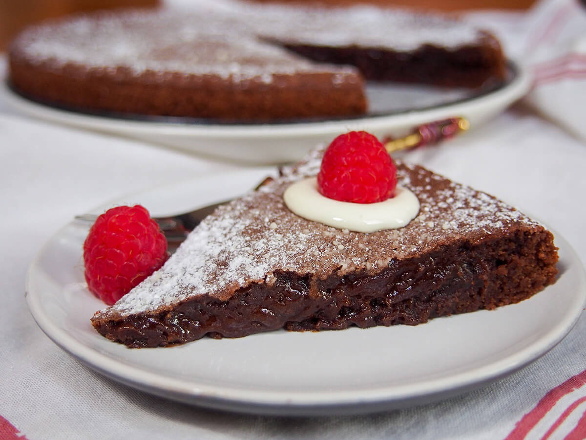 Kladdkaka is a wonderful Swedish chocolate cake that's crisp outside, sticky and gooey in the middle and packed with delicious flavor. Really easy and quick to make, it's a classic fika (coffee time) treat. slice of kladdkaka Swedish sticky chocolate cake on plate garnished with raspberries