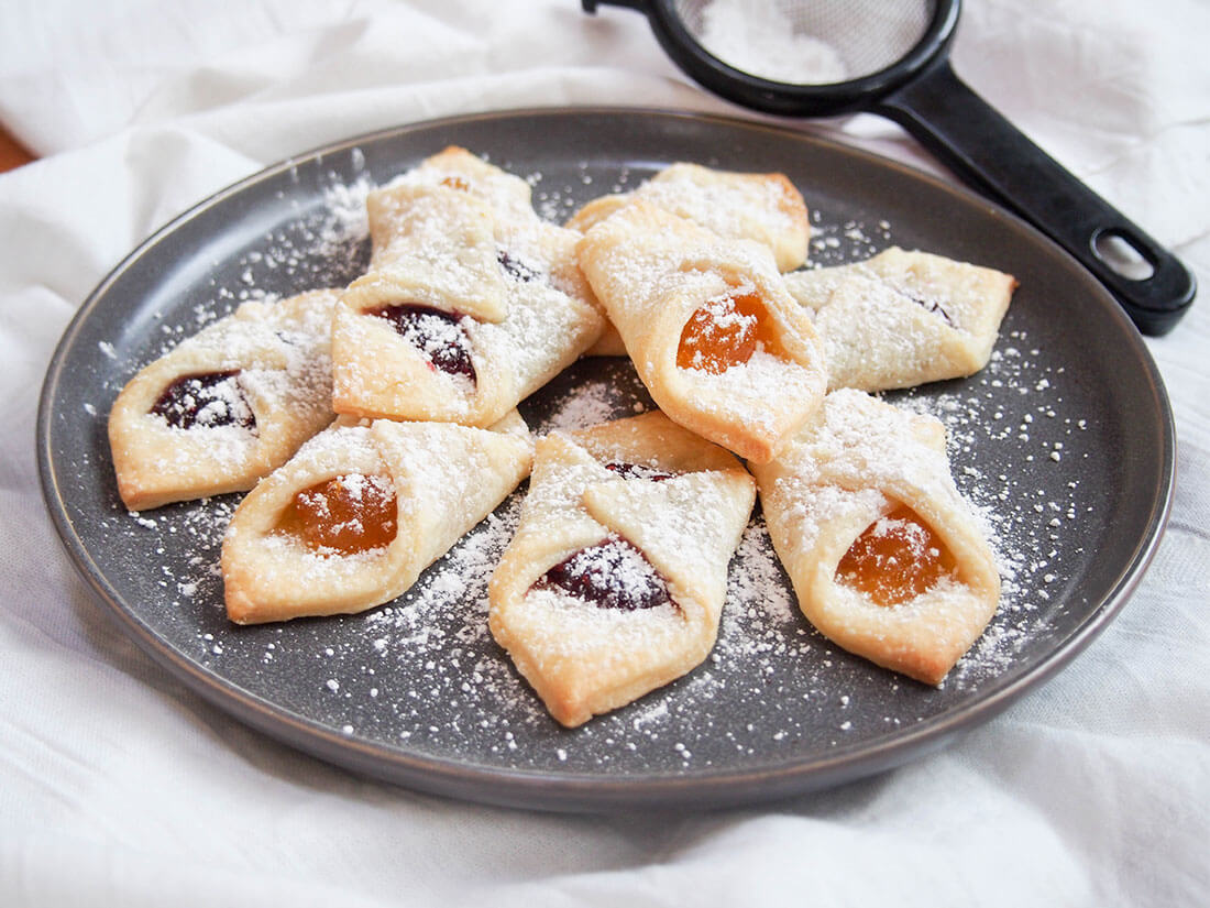 Kolachy cookies are an easy mix of a cream cheese pastry folded over a jam filling. They're as tasty as they are pretty, and a great addition to your cookie plate. kolachy cookies on plate, dusted with powdered sugar
