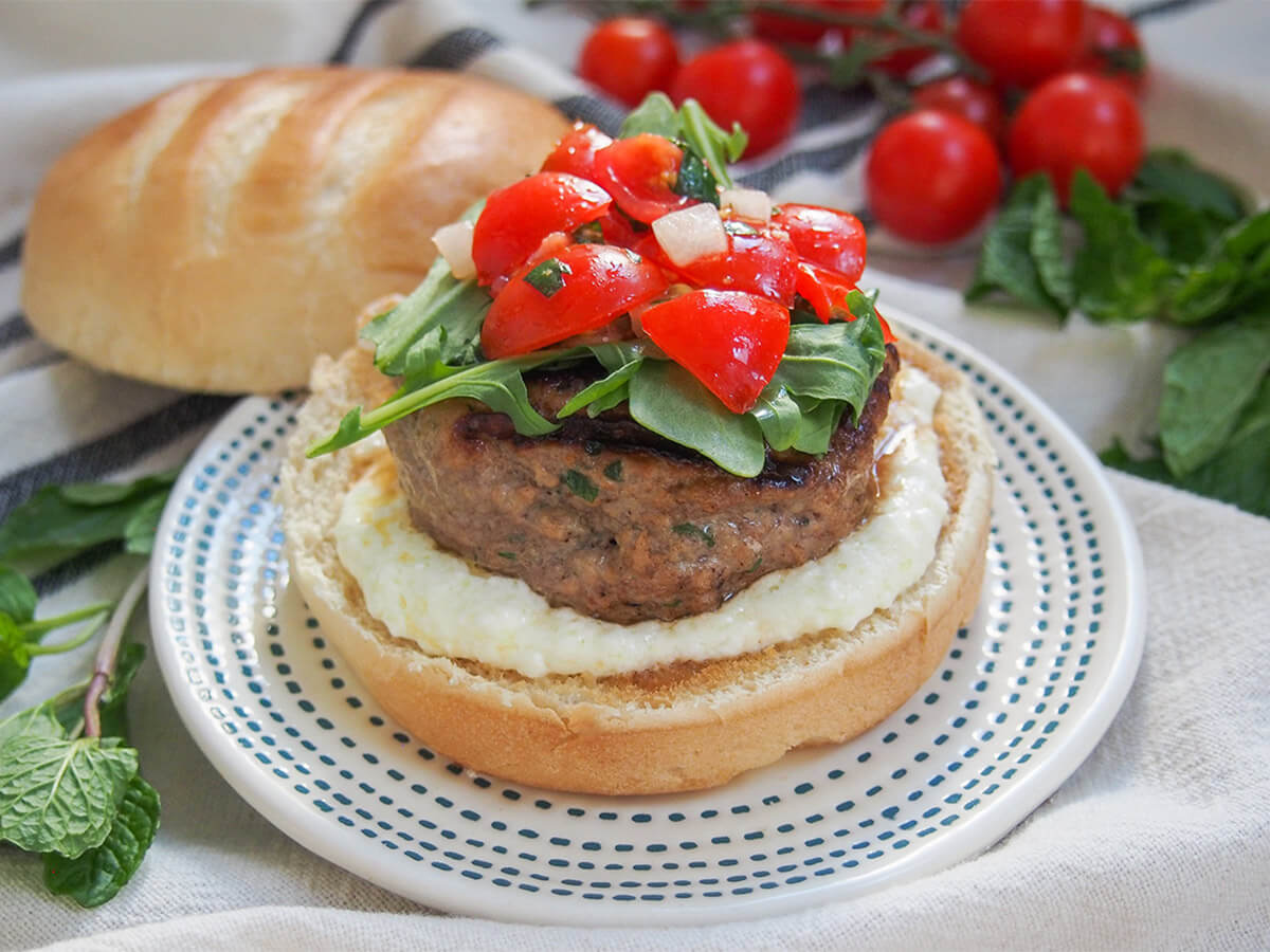 lamb burgers with feta sauce and tomato salsa lamb burger with feta sauce with top of bun behind plate