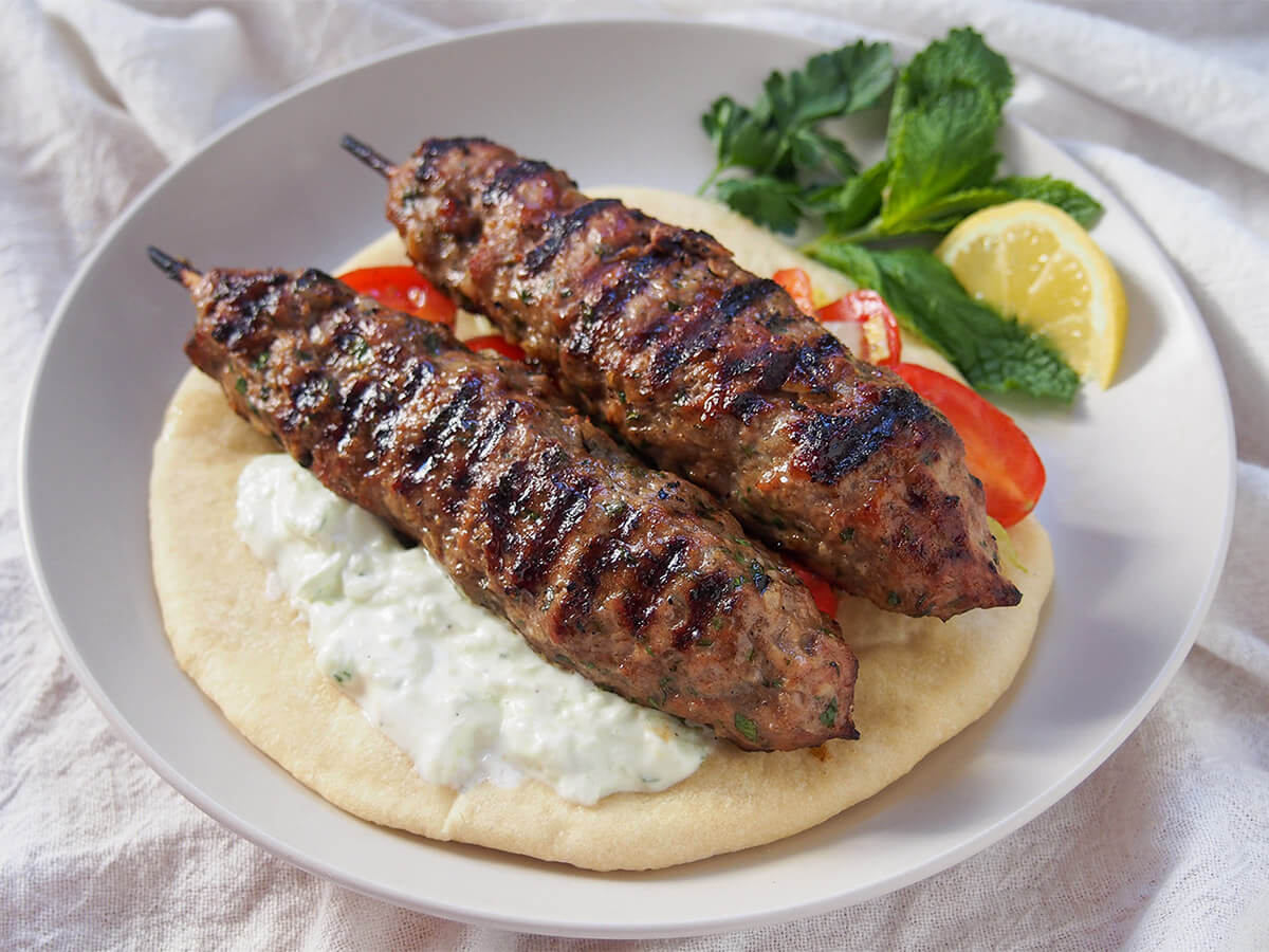 Lamb kofte (köfte) with cacik - a tasty seasoned ground lamb long meatball with cucumber-yogurt sauce lamb kofta or kofte on pita with cacik under kebab