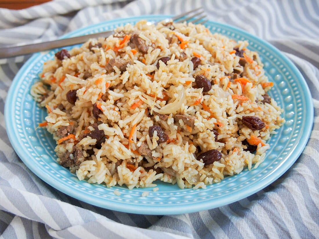 This delicious lamb pilaf, based on the traditional Afghan/Uzbek dish, is an easy, one pot meal but packed with flavor. plate of lamb pilaf with fork at back of plate