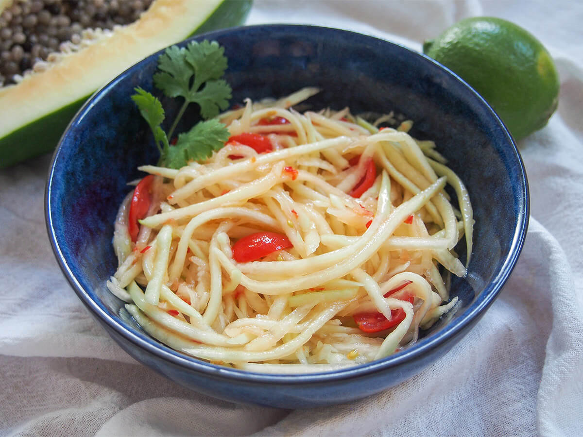 Green papaya salad is a refreshing, tasty side or appetizer with other Thai and Laos dishes. Easy to make & with great sweet-spicy-umami flavors. bowl of Lao green papaya salad with lime behind