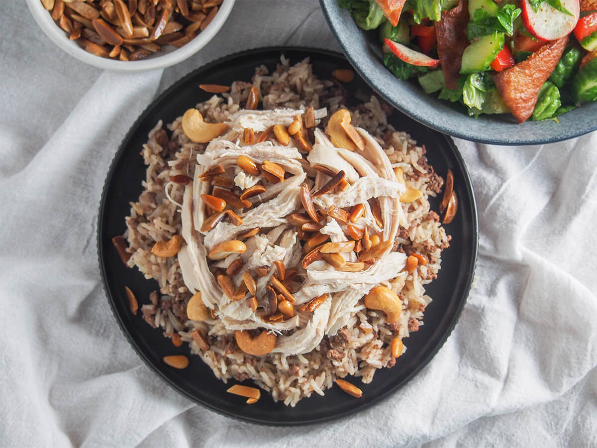 Lebanese chicken and rice is a delicious combination of luscious rice cooked with ground meat and spices, shredded chicken and toasted nuts. It's a dish packed with great flavors and textures. plate of Lebanese chicken and rice from overhead with bowl of salad above