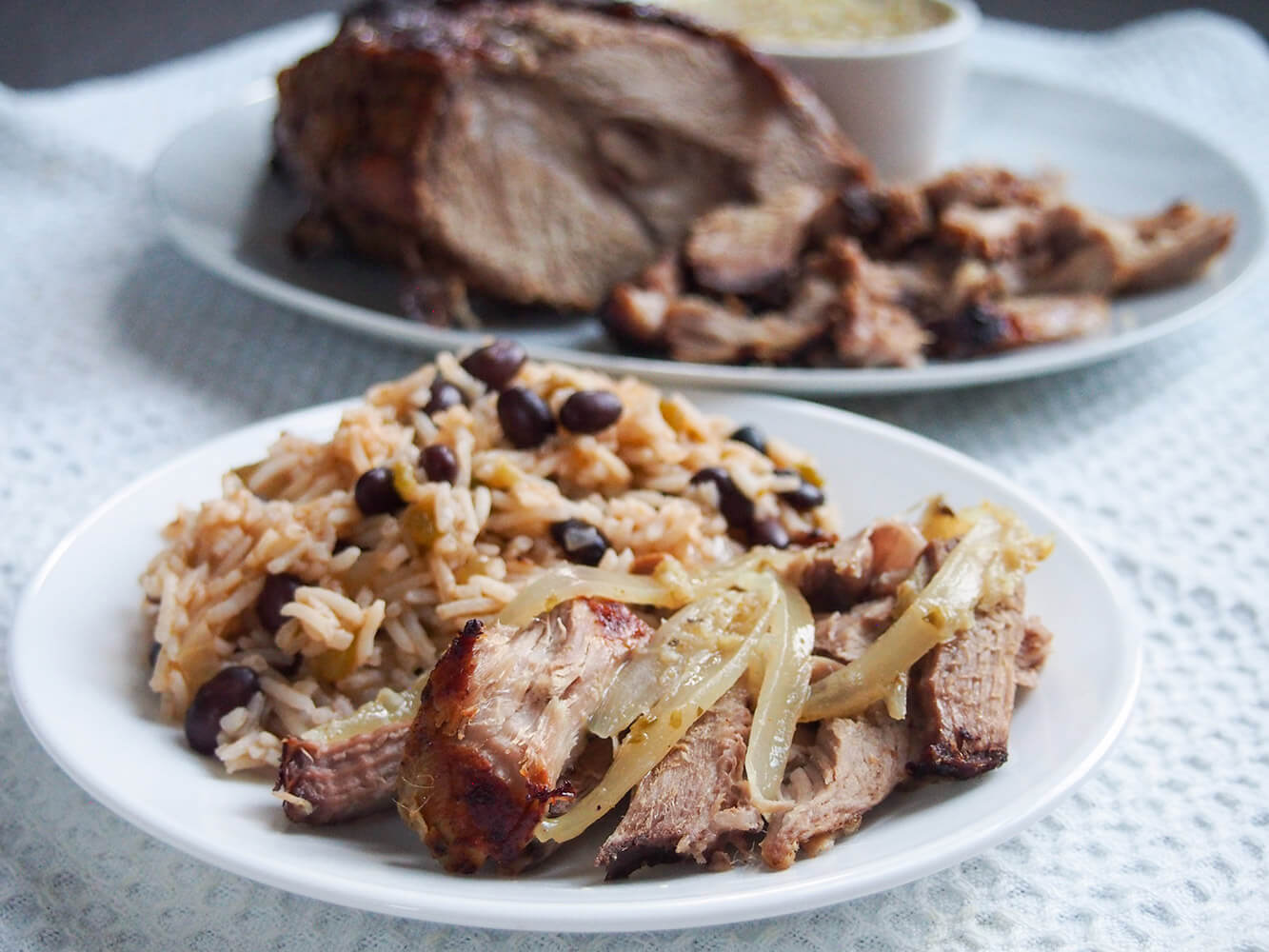 This Cuban roast pork, lechon asado, is packed with delicious flavors thanks to the citrus and garlic mojo marinade. It's easy to make and delicious for dinner plate with lechon asado topped with mojo sauce and onions, served with rice and black beans