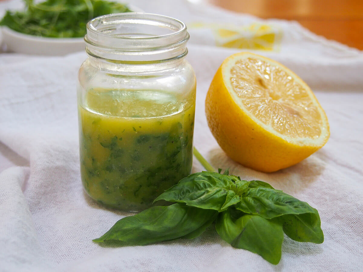 This lemon basil vinaigrette is easy to make with just a few ingredients & has a wonderful bright flavor. It's perfect for salads, drizzled on fish & more. jar of lemon basil vinaigrette with half lemon and sprig of basil to side