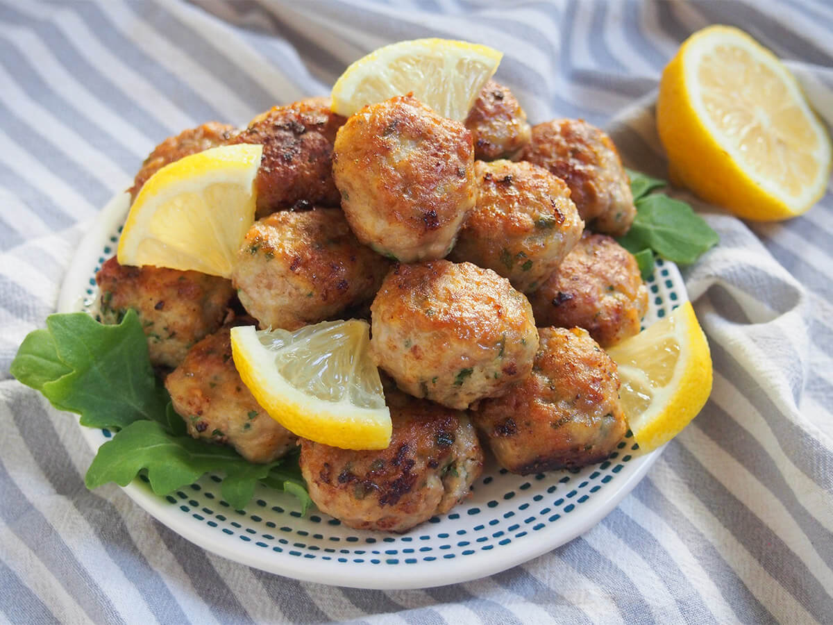 These lemon pork meatballs are based on Italian polpette al limone and made with lemon and parmesan, giving them a brightness and tasty flavor. They're quick and easy to make and great as an appetizer or main. plate of lemon pork meatballs with part lemon behind