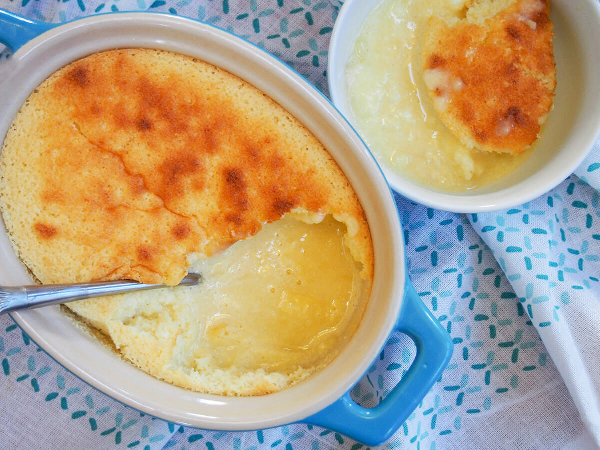 This lemon pudding cake is so easy to make and the result is so comforting with a wonderful lemon tang. The mixture separates slightly during baking to give a sponge-like mixture on the top and creamy sauce on the bottom. No wonder it also goes by the name lemon delicious. lemon pudding cake in dish with bowl with some to side
