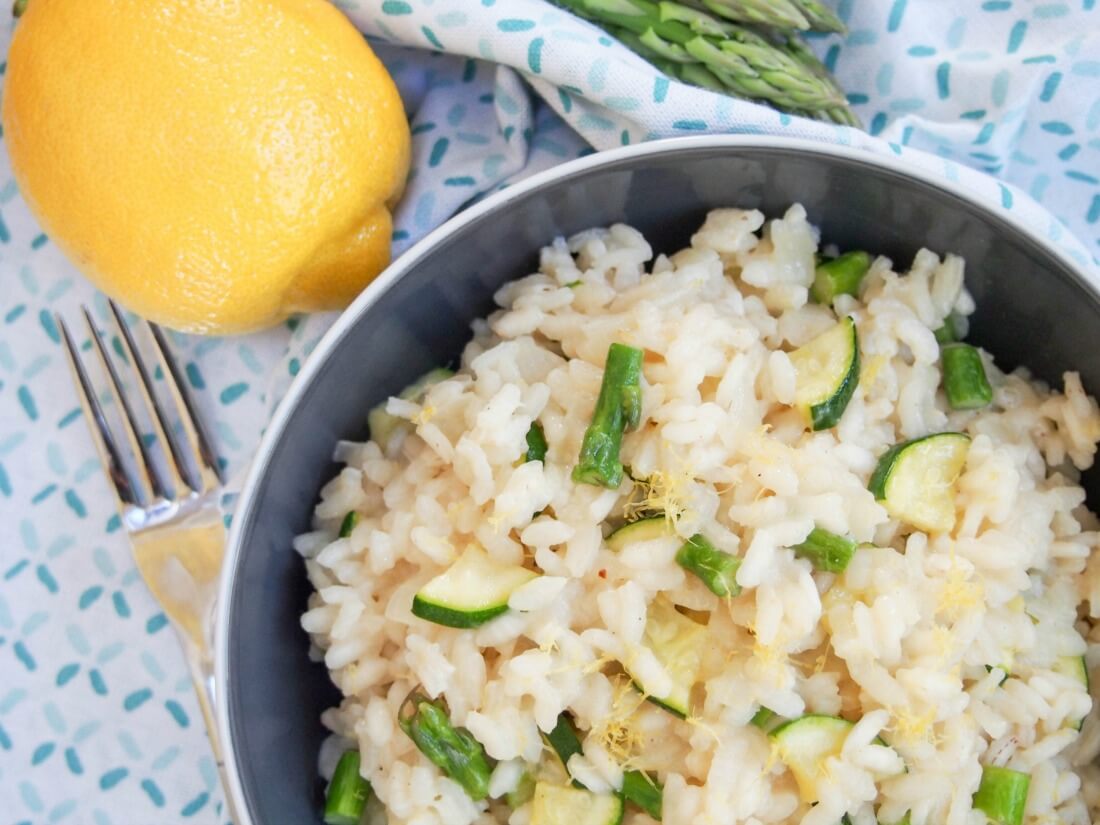 Lemon risotto has all the comfort factor you'd expect in a risotto, with the fresh flavors of spring. It's lighter and brighter, and a delicious meal. part view of bowl of lemon risotto with asparagus and zucchini with fork to side and lemon beside bowl
