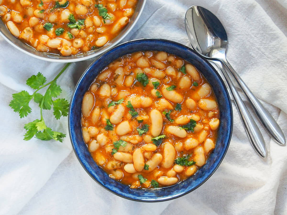 bowl of Moroccan stewed white beans bowl of loubia Moroccan white bean stew from overhead with two spoons to right side