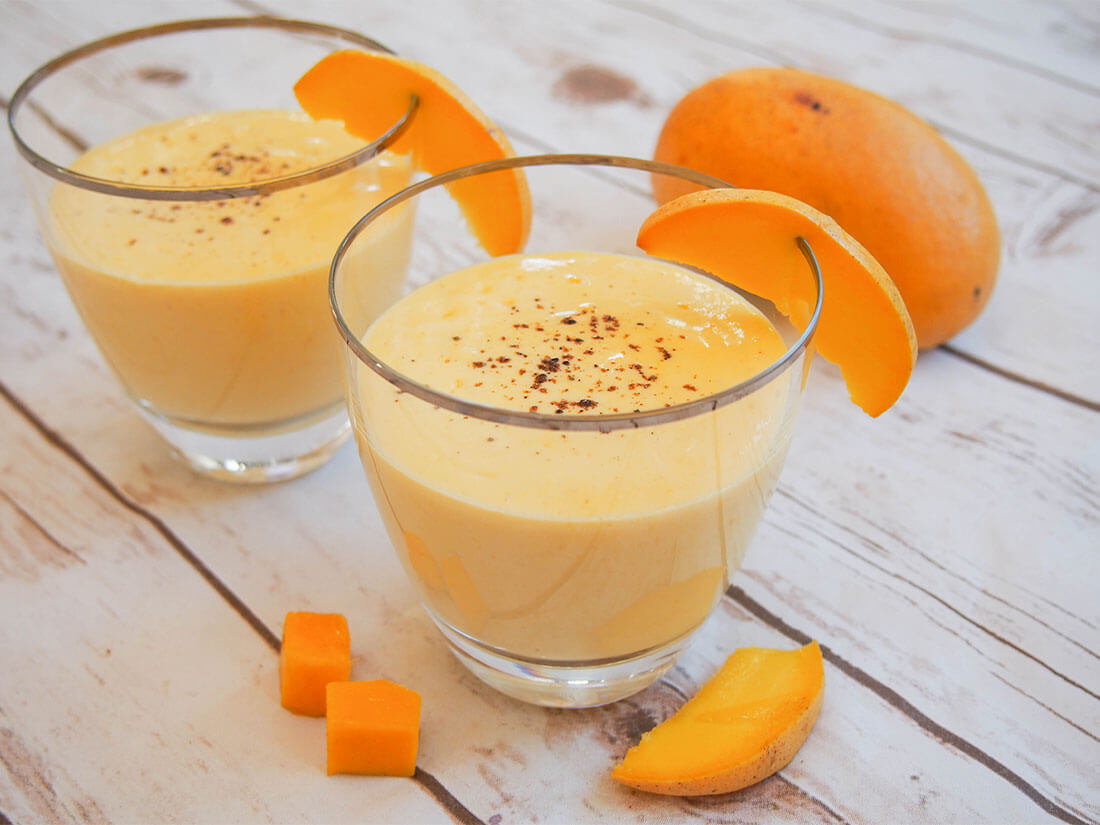 Mango lassi is the simplest Indian mango smoothie that's smooth, creamy and delicious. It's super easy and perfect any time. two glasses of mango lassi with pieces of mango to side