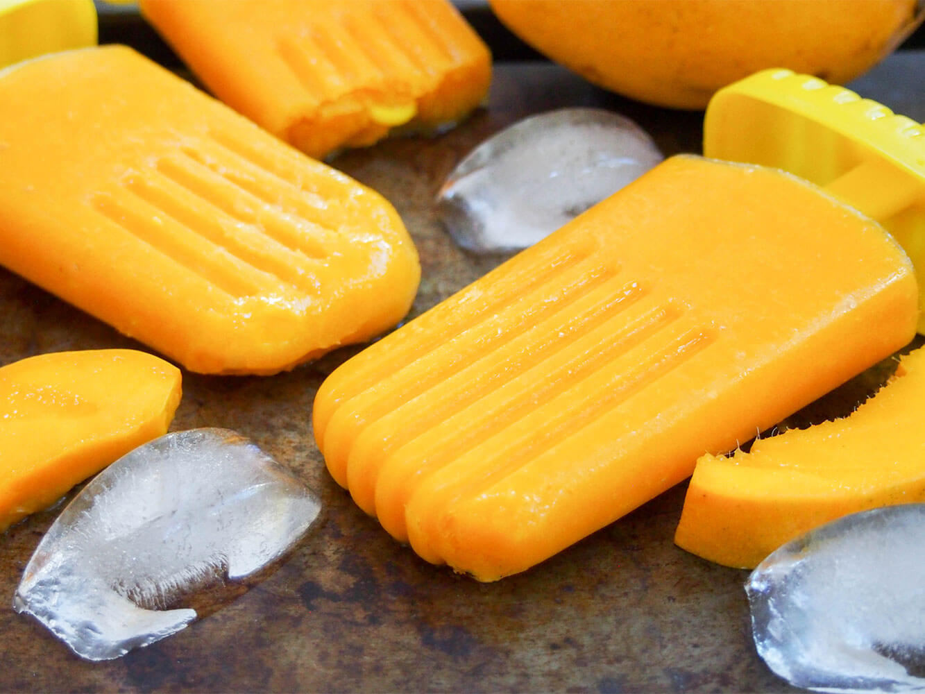 If you're looking for an easy and relatively healthy way to cool down, these mango paletas are perfect. They have only 3 ingredients and not a lot of sugar for ice cold, fruity deliciousness that's a true taste of summer! mango palatas (ice pops) on tray with ice to side