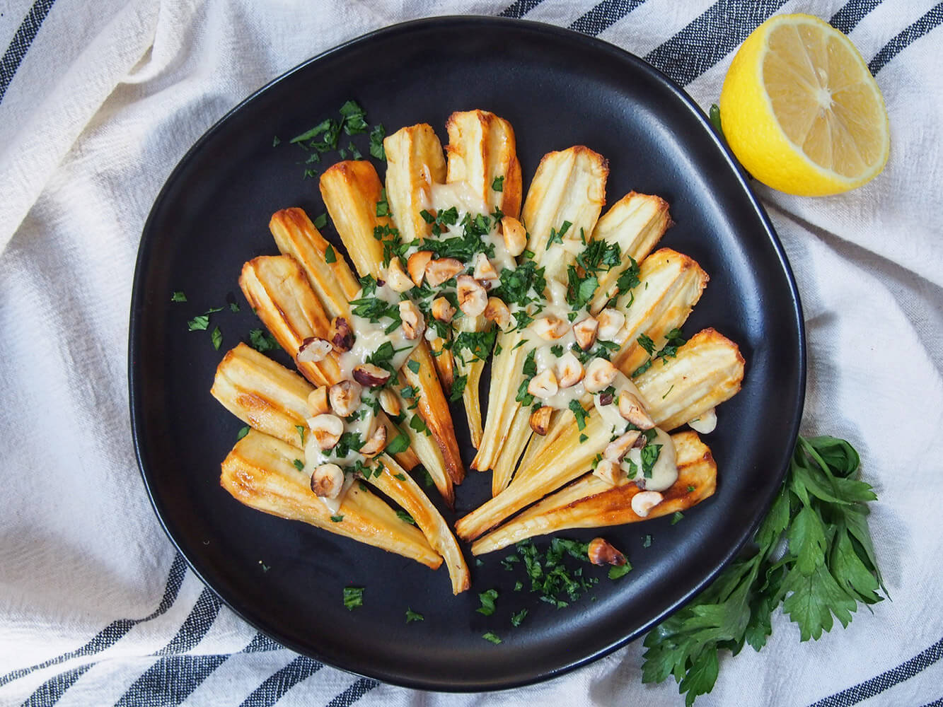 Enjoy these elegant, easy and delicious maple roasted parsnips, topped with a creamy tahini dressing and crunchy toasted hazelnuts. It's a wonderful combination that makes a pretty and tasty change to your usual veg. plate of maple roasted parsnips from overhead