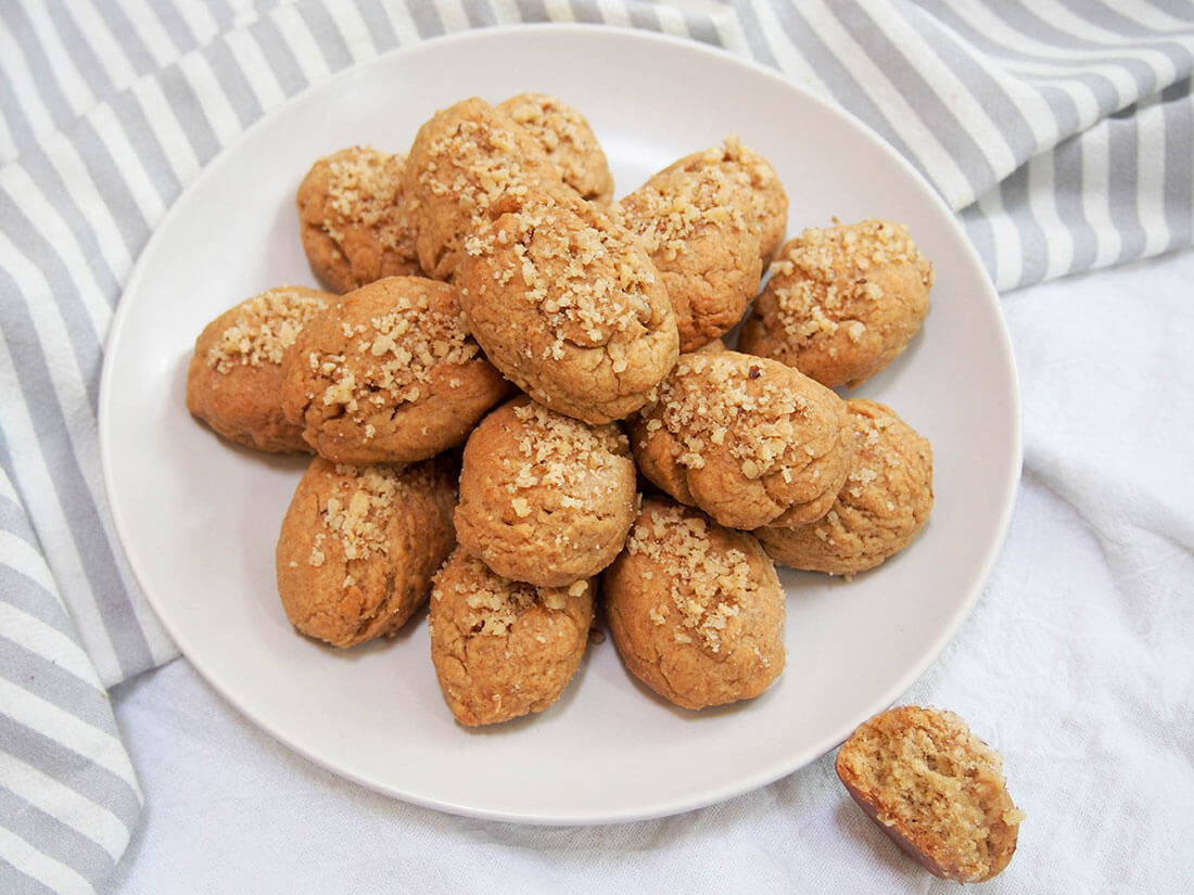 Melomakarona are a classic Greek cookie, with a gently spiced flavor in the dough and finished by dipping them in honey syrup. plate of melomakarona (Greek honey cookies) with one to side