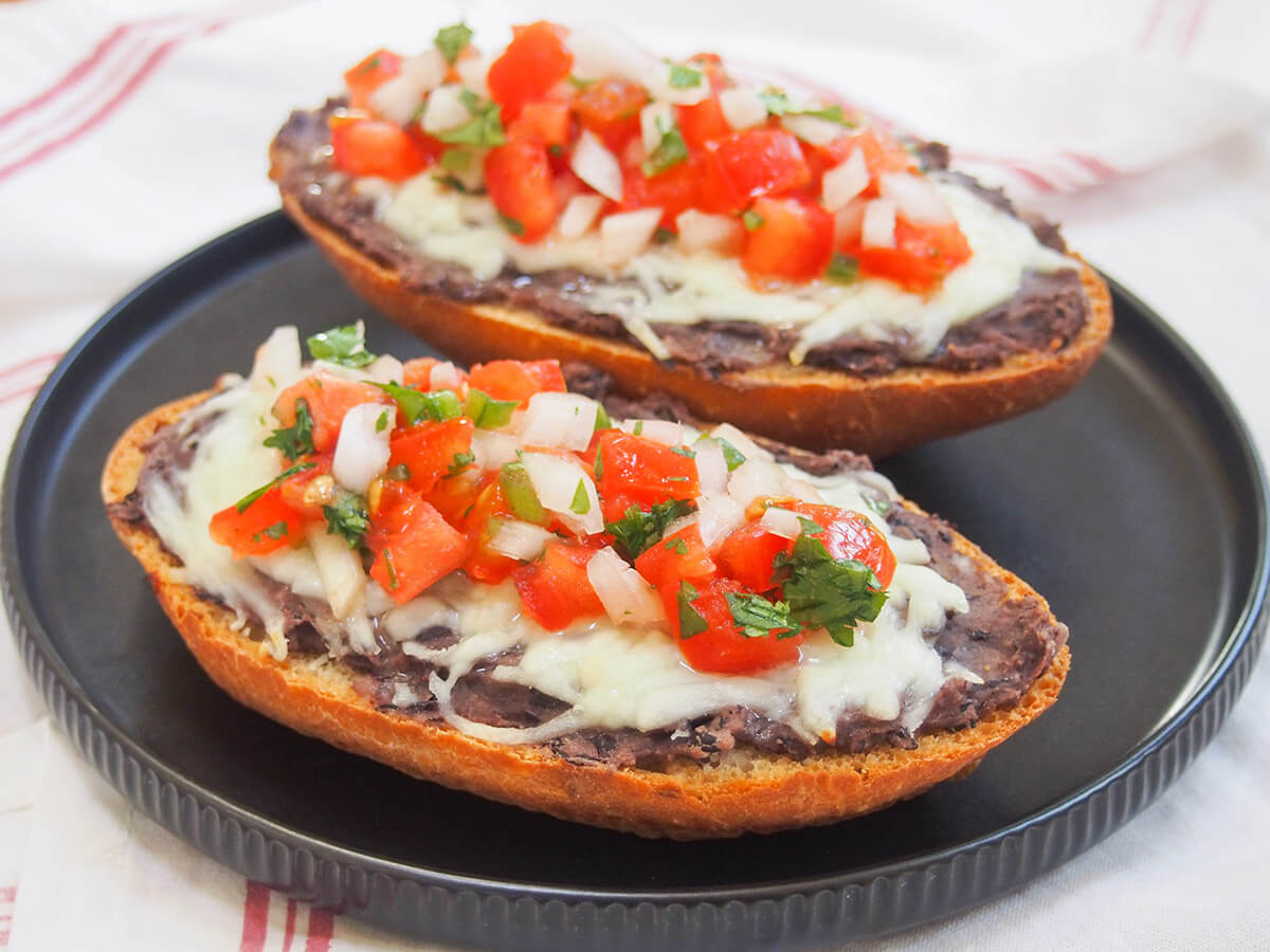 Breakfast (or any meal, to be honest) can hardly get more comforting than this easy and delicious Mexican creation. Molletes loads cheese, beans and salsa on bread and is as tasty as it sounds. black plate with two pieces of Mexican molletes on top