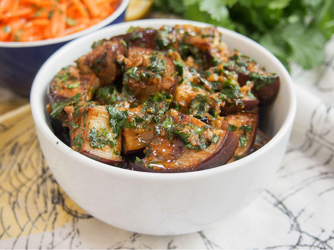 If you ever thought eggplant was boring, then you need to try this Moroccan eggplant with chermoula. The punchy sauce transforms cooked eggplant to make a flavor-packed side or mezze dish. Moroccan eggplant with chermoula in bowl with carrot salad behind