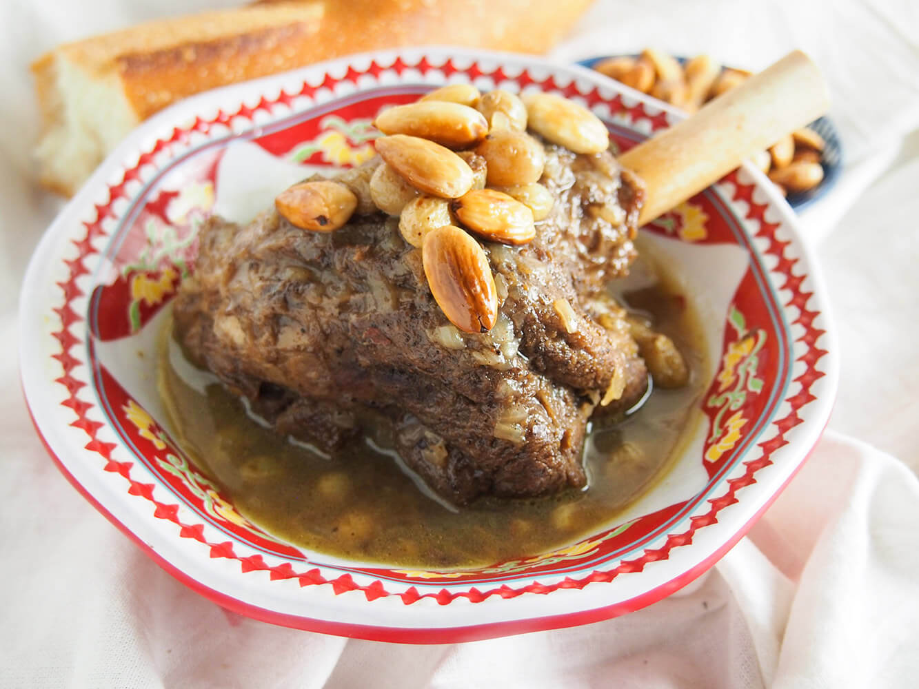 Mrouzia is a delicately flavored, slow cooked Moroccan lamb tagine with warm spice flavors, tender meat and topped with sweet soft raisins and crunchy toasted almonds. It's a comforting dish, that's also easy to make. mrouzia honey lamb tagine in bowl topped with toasted almonds