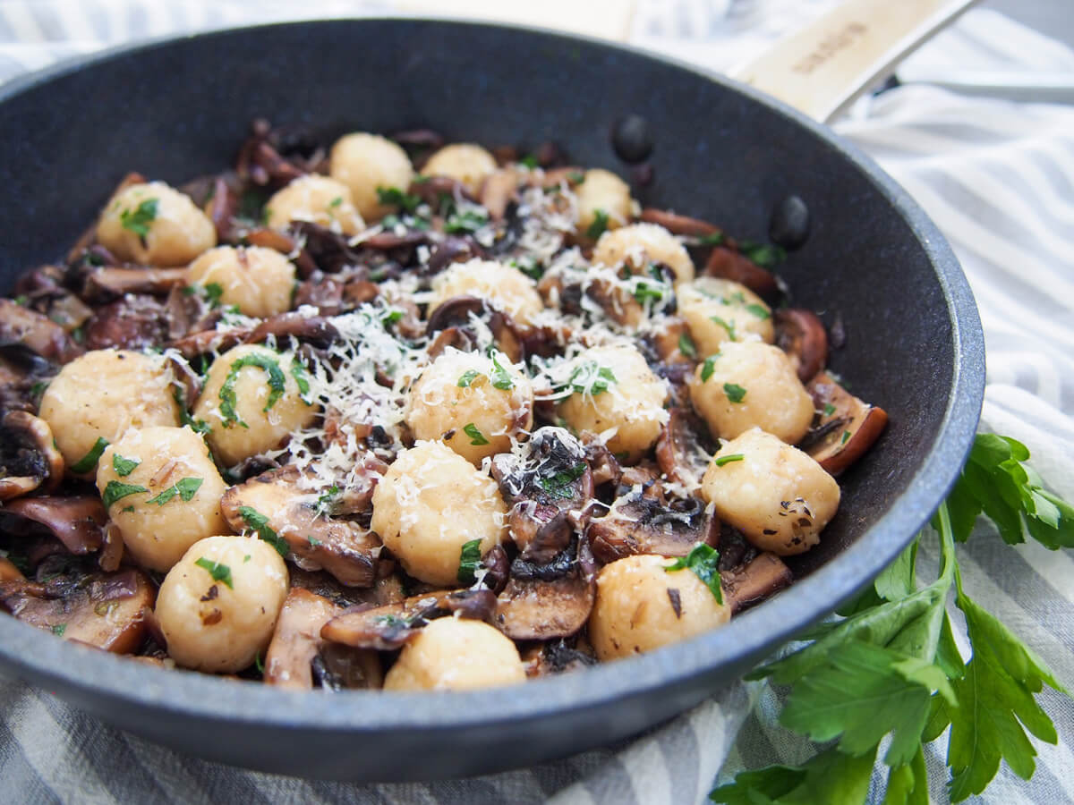 This mushroom gnocchi is a comforting, tasty way to make gnocchi go further. It's quick, easy and packed with earthy flavors. A tasty vegetarian meal that will win over anyone. mushroom gnocchi in skillet with parsley sprig to side