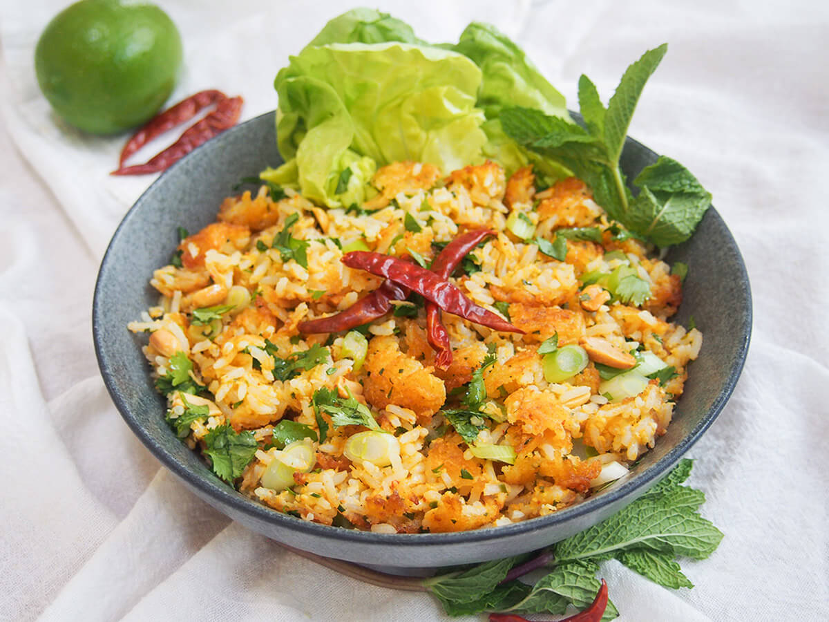 Nam khao is a delicious Lao salad made by frying balls of seasoned rice then breaking them up and mixing with herbs, peanuts and more. It's a wonderful mix of flavors (including a bit of spice and sour) and has great textures. Delicious as a light meal or side. bowl of nam khao Lao crispy rice salad with lime and chilis behind bowl