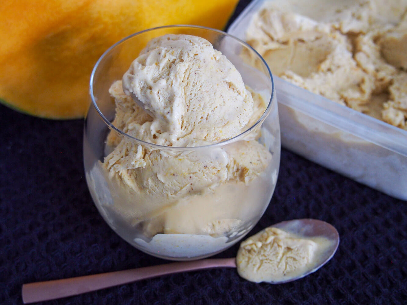 This no churn pumpkin ice cream is a wonderful combination of real pumpkin, a little warm spice and a wonderfully creamy base. It's really easy to make and perfect for those warmer fall days, or any excuse. glass of no churn pumpkin ice cream with spoon under and tub behind