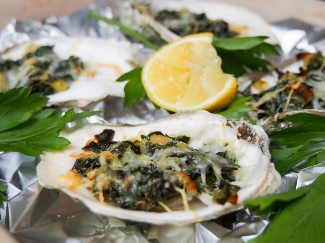 Oysters Rockefeller are a classic New Orleans appetizer with a tasty topping baked over oysters in their shell. Here they're lightened up but packed with flavor. close up of oysters Rockefeller with lemon slice behind