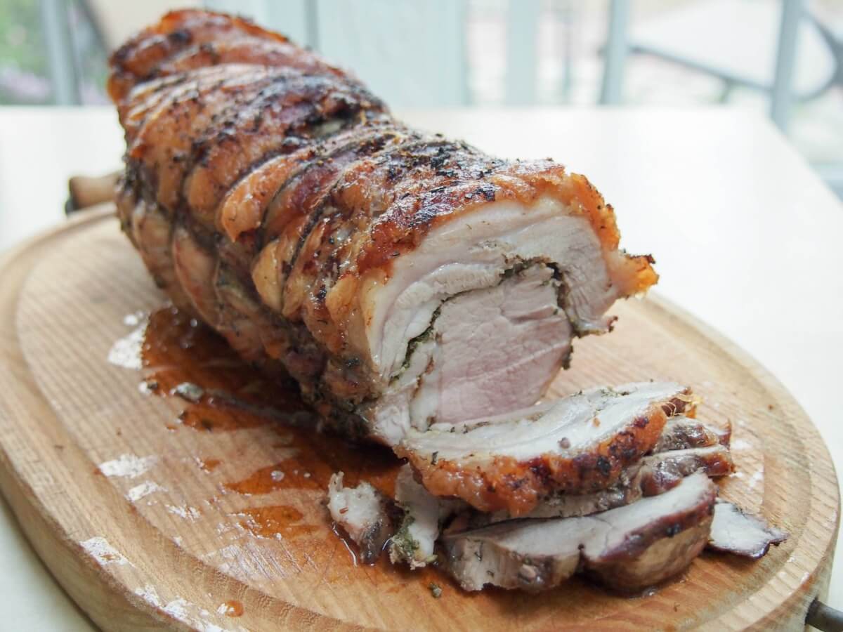 Porchetta is a classic Italian pork roast, great in sandwiches. Left to infuse with herbs, fennel and salt overnight, the flavor is delicious, the fat crisp. whole porchetta on cutting board with a few slices cut from front