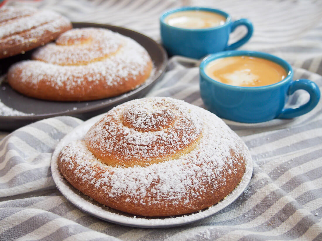 Pan de Mallorca are an egg-rich but light, gently sweet bread roll from Puerto Rico. They're easy to recognize, coiled up and dusted with sugar, and make a delicious breakfast or snack. Pan de Mallorca (Puerto Rican sweet rolls) - one on plate with more behind