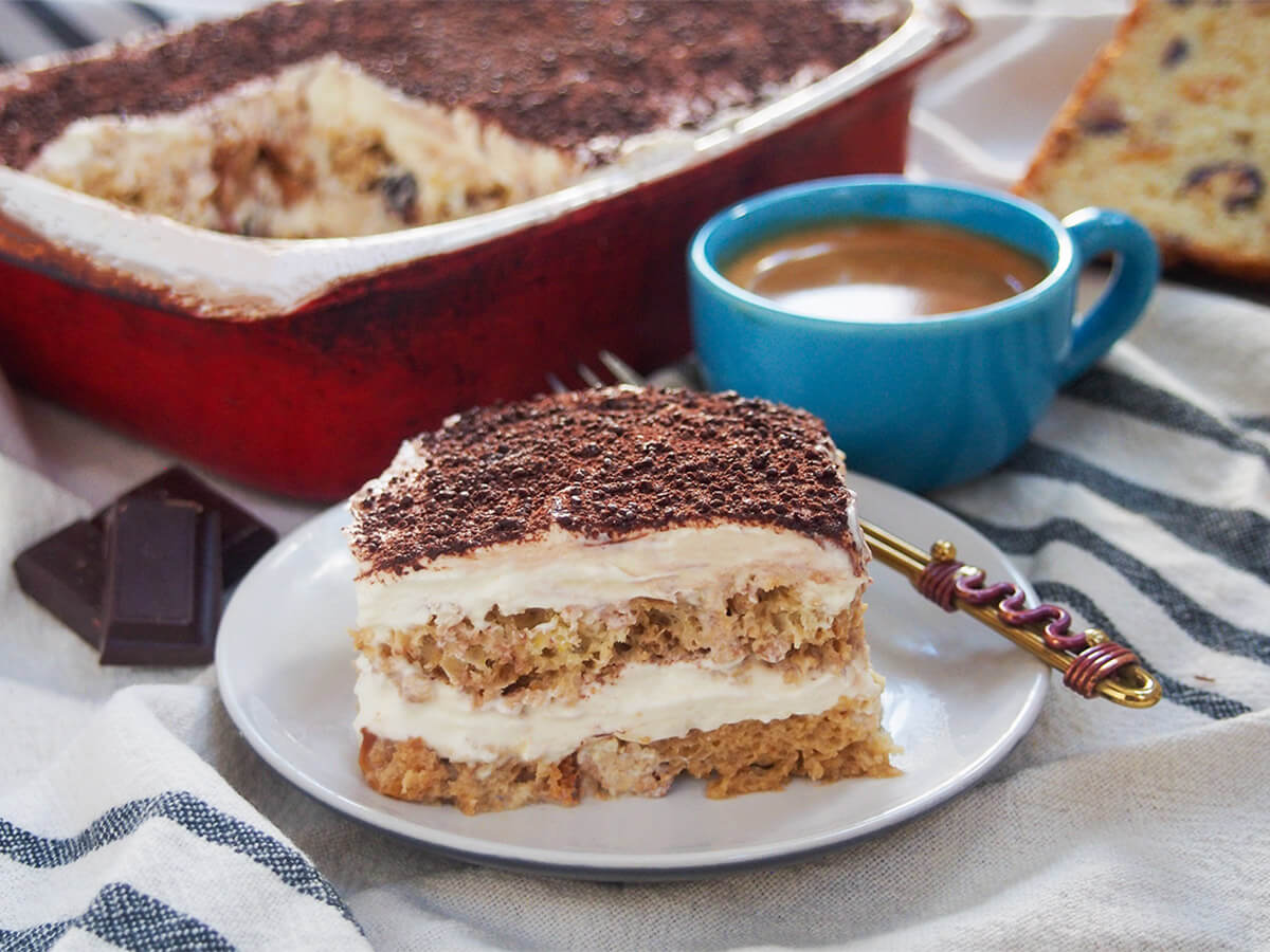 piece of panettone tiramisu on plate slice of panettone tiramisu in front of rest of dish and cup of espresso coffee.