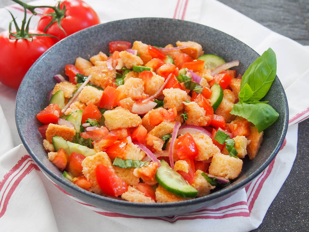 This panzanella salad is such a delicious taste of summer. It's easy to make, frugal and packed with flavor. bowl of panzanella salad viewed from side with basil garnish