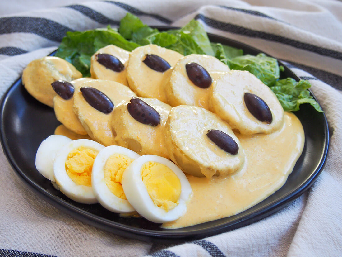 Papa a la Huancaina is a classic Peruvian appetizer of potatoes smothered with a delicious cheese and chili sauce. It's no doubt unusual if you're not familiar with it, but the flavors are incredibly tasty and it's easy too. Papa a la Huancaina on plate served with hard boiled egg and lettuce