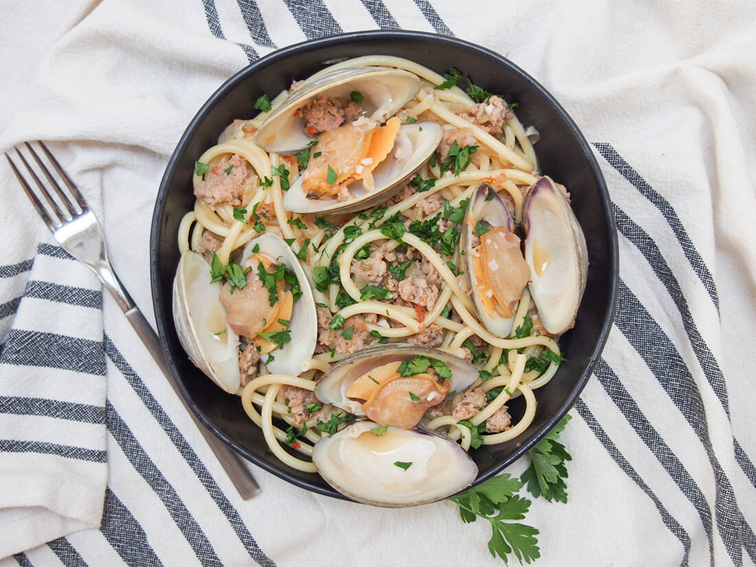 With a bit of a kick from the spicy sausage and delicate clams, all tied together with wine and garlic and delicious pasta, this pasta with clams and sausage is an easy fancy-feeling meal! Pasta with clams and sausage in bowl with fork to side viewed from overhead