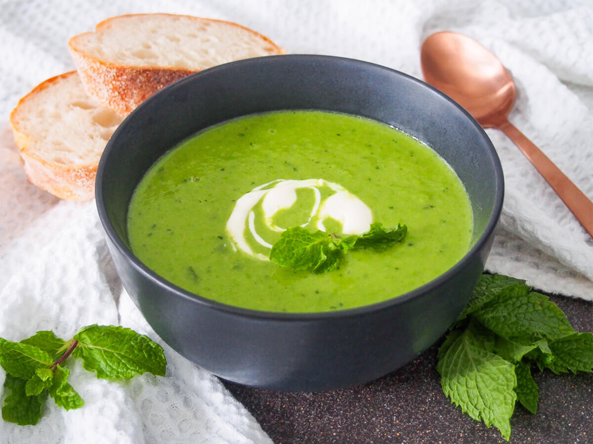 This pea and mint soup is a true taste of spring, with its bright green color and light flavors. It's also incredibly quick and easy to make using fresh or frozen peas. Serve warm or chilled. bowl of pea and mint soup with spoon and bread behind and mint sprigs to side of bowl