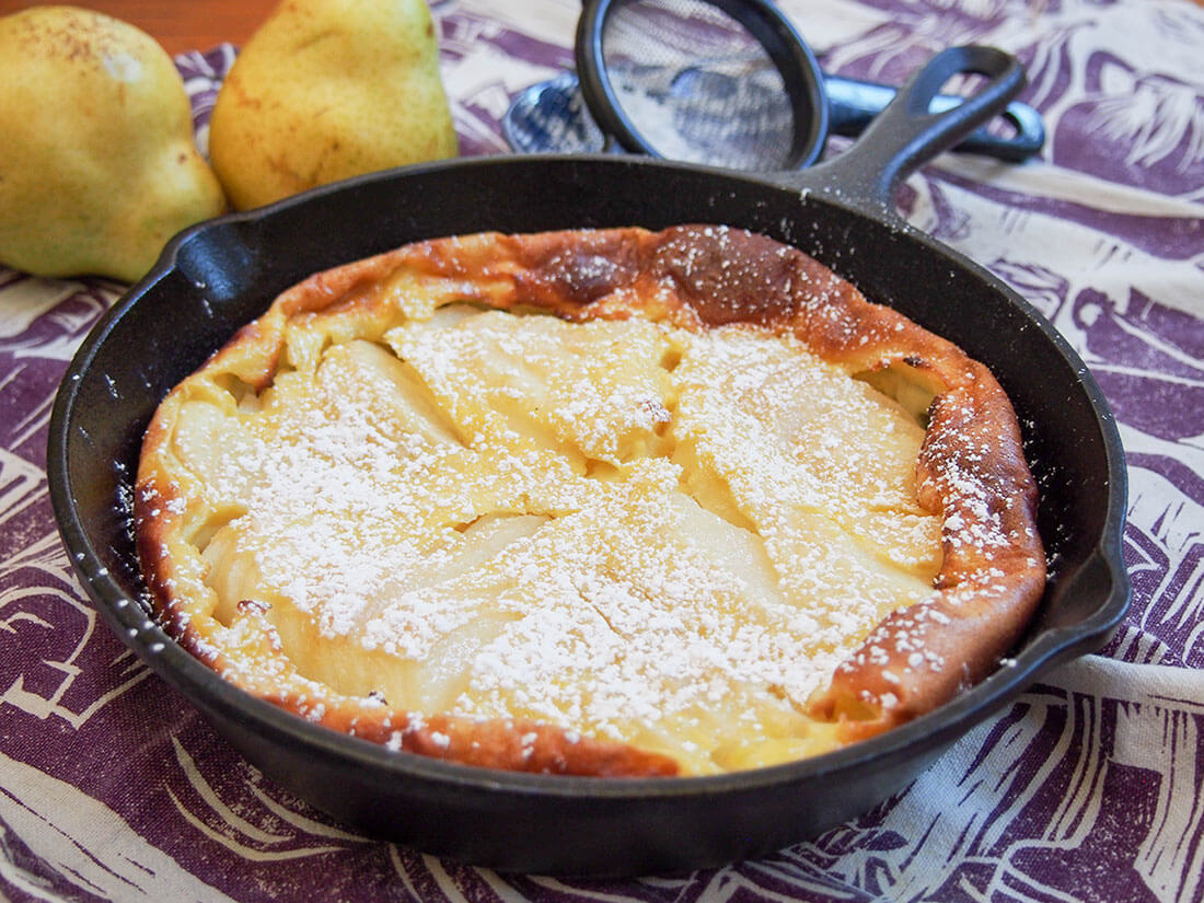 This pear clafoutis combines tender, sweet pears with a custard-like base for a comforting treat. It's an easy, delicious dessert. Pear clafoutis in skillet, dusted with sugar, with pears behind