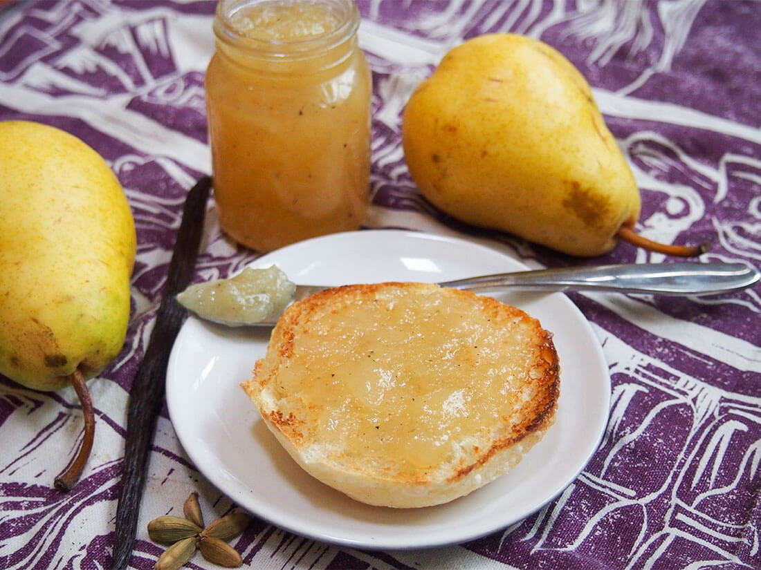This pear jam is flavored with a hint of vanilla and cardamom that add a hint of warmth but let the pear flavors shine. Easy and delicious! pear jam on piece of bread with jar behind