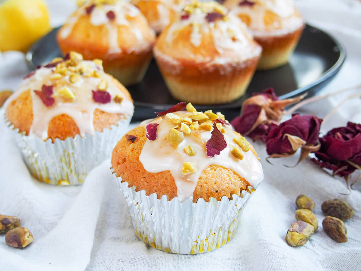 These Persian love cake cupcakes are the perfect way to enjoy the wonderful flavors in individual servings. Flavored with the classic Persian flavors of cardamom, rosewater and lemon, they are light, aromatic and delicious. two Persian love cake cupcakes in casing with more on plate behind