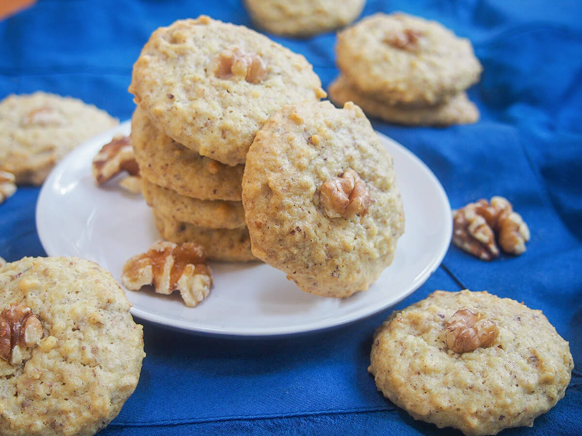 Persian walnut cookies - nan-e gerdui: These Persian walnut cookies have only 4 ingredients, are gluten free & easy to make. Traditionally for Nowruz, they're a tasty treat any time. stack of Persian walnut cookies with one to side and more cookies around plate