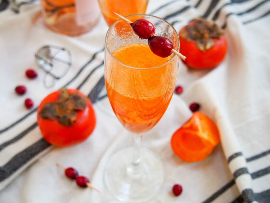 Only 3 ingredients, a couple minutes and you've got a beautiful, bubbling glass perfect for any occasion. Make a persimmon apple cider mimosa your go-to seasonal cocktail. glass of persimmon apple cider mimosa with persimmon and cranberries around glass