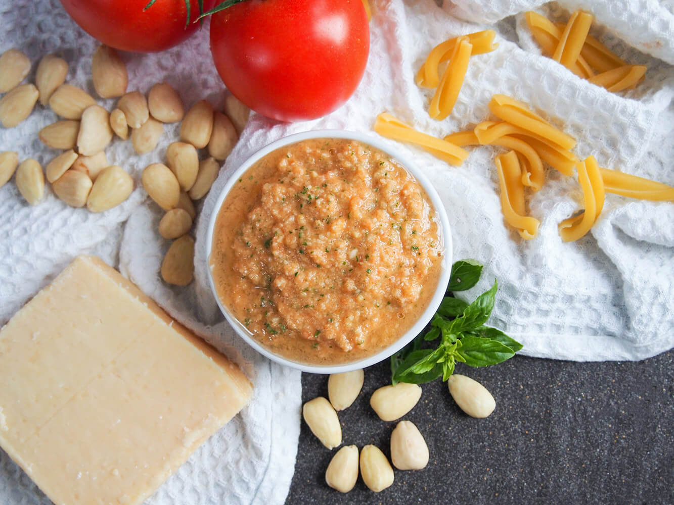 Pesto alla Trapanese is a Sicilian sauce made with almonds and raw tomato. It's fresh, bright and so easy to make. It makes a wonderful quick and simple pasta meal, perfect for summer. Pesto alla Trapanese in dish from overhead with ingredients around it