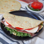 filled and folded piadina Italian flatbread on plate with tomato and additional un-filled flatbread behind