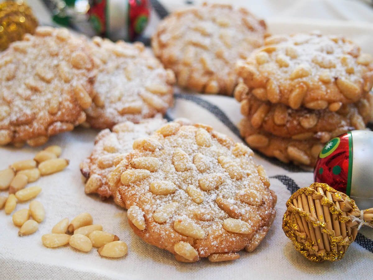 Pignoli are Italian pine nut cookies, with a sweet, chewy almond cookie base studded with crunchy pine nuts. They are easy to make, naturally gluten free and deliciously good. pignoli cookies dusted with powdered sugar with decorations to side
