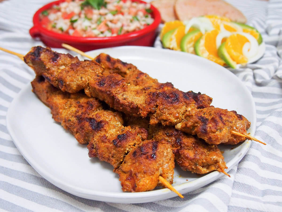 Pinchos morunos are Spanish pork skewers with an aromatic spice marinade. They're easy to make, full of flavor and the perfect tapas dish to add to your next party or get-together. plate of pinchos morunos Spanish pork skewers with salads behind